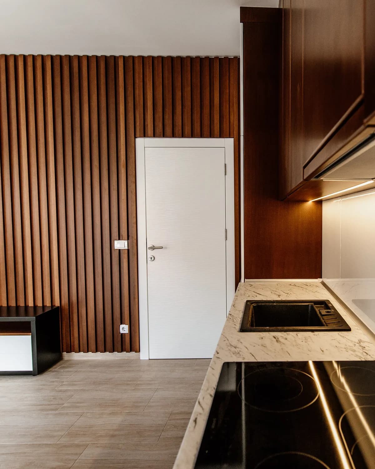A newly finished, empty open-plan room with a fitted kitchen and a wooden slatted wall